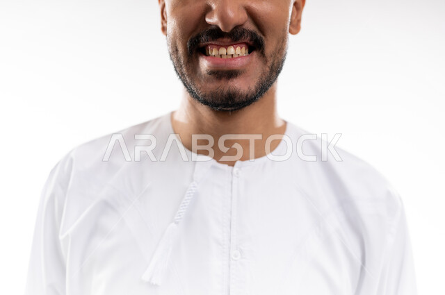 الاشارة إلى الفم بإيماءات الانزعاج والألم، مشاكل التهاب اللثة والحاجة لزيارة طبيب الأسنان, بورتريه  لشاب عربي خليجي عماني يرتدي الدشداشة و الكمه يشير الى فمه بايماءات الحاجه الى تلقي العلاج، خلفية بيضاء