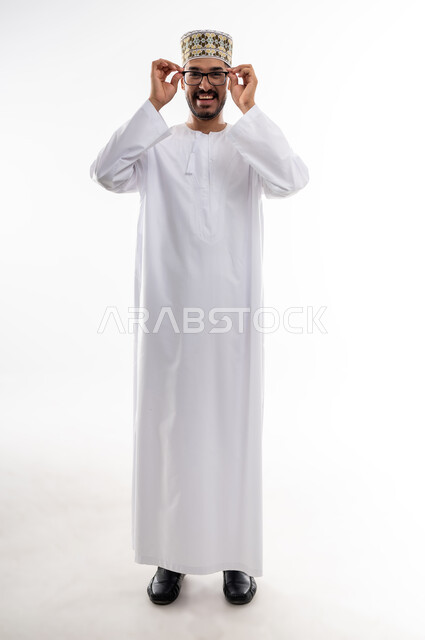 مفهوم طول النظر وقصره، الشعور بالسعادة والفرح بوضوح الرؤية, استخدام النظارة الطبية لتصحيح البصر, بورتريه لرجل عربي خليجي عماني يرتدي الدشداشه والكمه يمسك نظارته بيديه بايماءات استخدام الوسائل المساعده على النظر باستخدام النظارات الزجاجيه الطبيه، خلفيه بيضاء