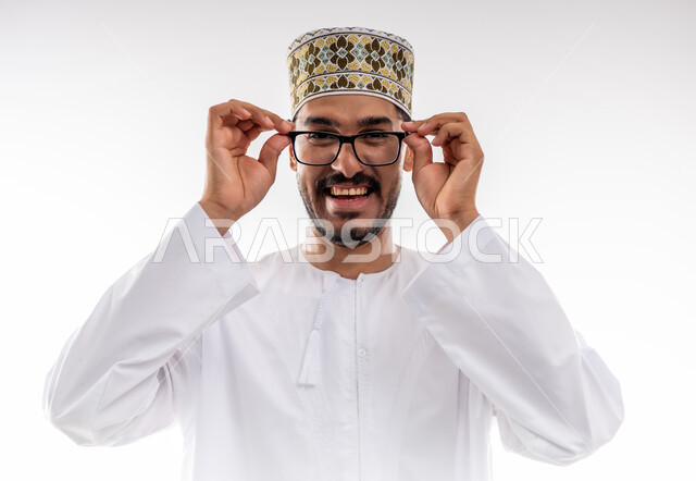 مفهوم طول النظر وقصره، الشعور بالسعادة والفرح بوضوح الرؤية, استخدام النظارة الطبية لتصحيح البصر, بورتريه لرجل عربي خليجي عماني يرتدي الدشداشه والكمه يمسك نظارته بيديه بايماءات استخدام الوسائل المساعده على النظر باستخدام النظارات الزجاجيه الطبيه، خلفيه بيضاء