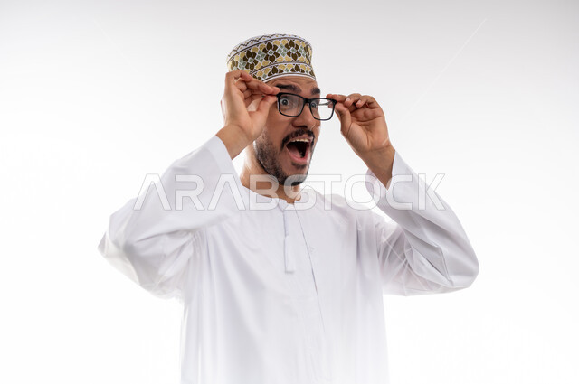 مفهوم طول النظر وقصره، الشعور بالسعادة والفرح بوضوح الرؤية, استخدام النظارة الطبية لتصحيح البصر, بورتريه لرجل عربي خليجي عماني يرتدي الدشداشه والكمه يمسك نظارته بيديه بايماءات استخدام الوسائل المساعده على النظر باستخدام النظارات الزجاجيه الطبيه، خلفيه بيضاء