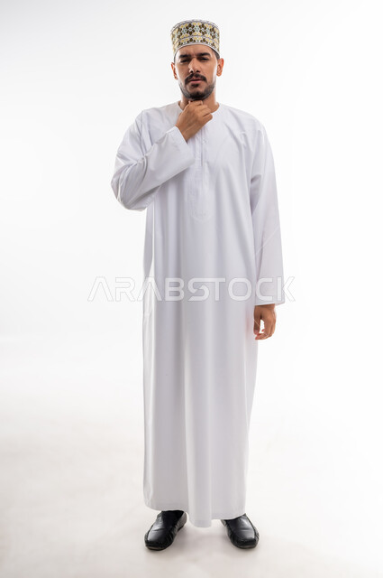 الاحساس بألم البلعوم والحاجة إلى العلاج والدواء, مفهوم الاهتمام بالصحة, الاصابة بنزلة برد والتهاب الحلق, بورتريه لرجل عربي خليجي عماني يرتدي الدشداشه والكمه يضع يده على حلقه بايماءات الشعور بالم الحلق والاحتقان, خلفية بيضاء