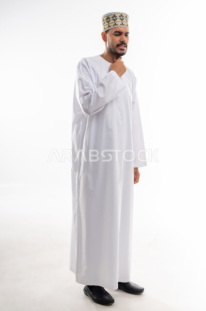 الاحساس بألم البلعوم والحاجة إلى العلاج والدواء, مفهوم الاهتمام بالصحة, الاصابة بنزلة برد والتهاب الحلق, بورتريه لرجل عربي خليجي عماني يرتدي الدشداشه والكمه يضع يده على حلقه بايماءات الشعور بالم الحلق والاحتقان, خلفية بيضاء