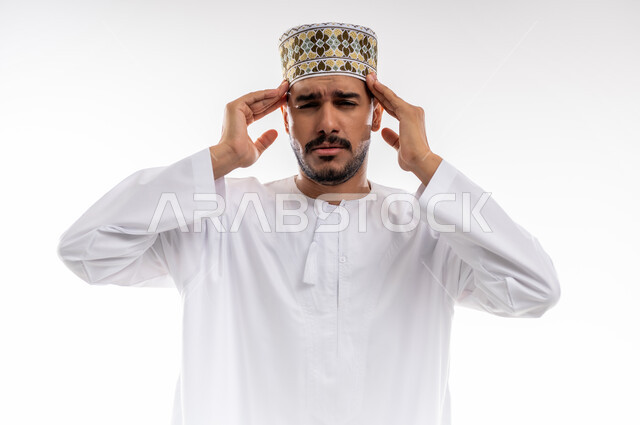 آلام شديدة في الرأس، ايماءات وجه ويدين تدلان على الشعور بالألم، بورتريه لرجل عربي خليجي عماني يرتدي الدشداشة والكمه يشير بيديه الى رأسه بأيماءات المرض والاحساس بالصداع والحاجه الى العلاج والراحه، خلفيه رماديه