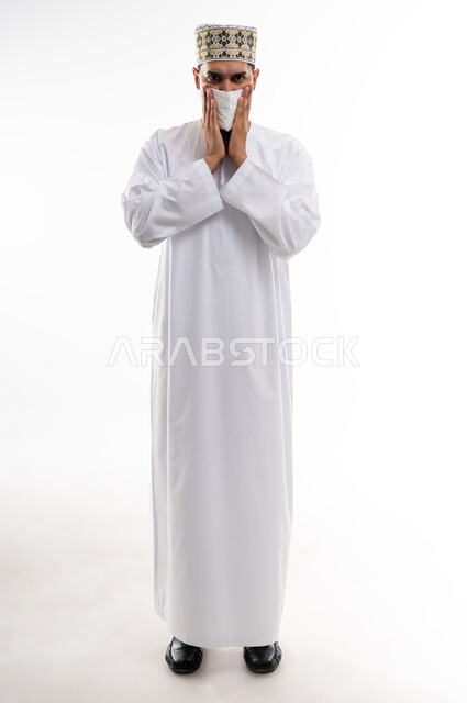 الشعور بالمرض و الزكام والحاجة الى العلاج، التهاب الأنف التحسسي، بورتريه لشاب عربي خليجي عماني يرتدي الدشداشة و الكمه يضع منديلا على أنفه بإيماءات العطاس والبرد والزكام, استخدام المناديل الورقيه, صوة الجسم بالطول الكامل، خلفية بيضاء