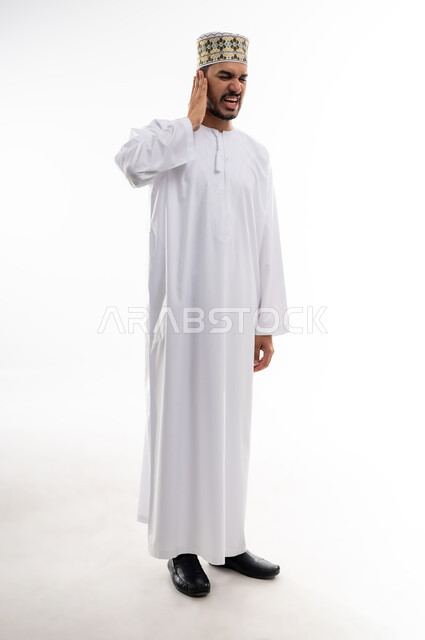 إلتهاب الاذن الحاد وضعف السمع، طلب العلاج والمساعده، بورتريه لرجل عربي خليجي عماني يرتدي الدشداشه والكمه يضع يده على أذنه بإيماءات تدل على الشعور بألم حاد في أذنه و الحاجه لزيارة الطبيب، خلفية بيضاء