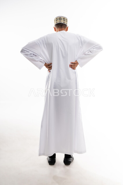 Nerve and muscle aches and pains, request for help and need for treatment, muscle and joint inflammation, portrait of an Arab Gulf Omani man wearing a dishdasha and a cuff, putting his hand on his waist with gestures of pain, fatigue and exhaustion, emergency medical case, gray background