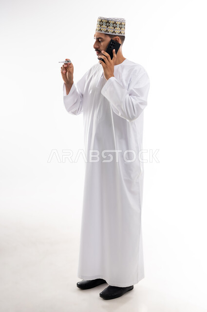 أعراض الاصابة بالحمى والتعب الجسدي وقياس درجه حراره الجسم،  بورتريه لرجل عربي خليجي عماني يرتدي الدشداشه والكمه يقوم بقراءه درجة حرارته باستخدام الميزان الحراري الرقمي, مفهوم الاهتمام بالصحة والحاجه الى العلاج, خلفية بيضاء
