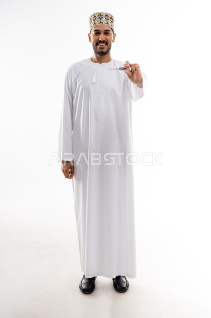 أعراض الاصابة بالحمى والتعب الجسدي وقياس درجه حراره الجسم،  بورتريه لرجل عربي خليجي عماني يرتدي الدشداشه والكمه يقوم بقراءه درجة حرارته باستخدام الميزان الحراري الرقمي, مفهوم الاهتمام بالصحة والحاجه الى العلاج, خلفية بيضاء