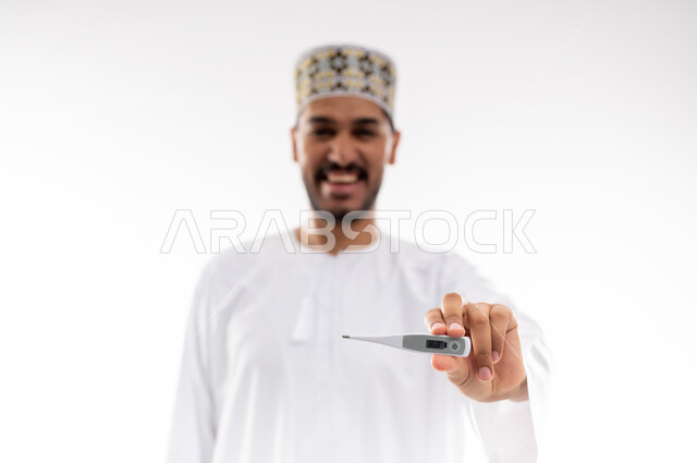 أعراض الاصابة بالحمى والتعب الجسدي وقياس درجه حراره الجسم،  بورتريه لرجل عربي خليجي عماني يرتدي الدشداشه والكمه يقوم بقراءه درجة حرارته باستخدام الميزان الحراري الرقمي, مفهوم الاهتمام بالصحة والحاجه الى العلاج, خلفية بيضاء