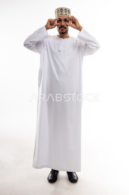 الوقوف امام الكاميرا وأداء حركات تمثيليه، بورتريه لرجل عربي خليجي عماني يرتدي الدشداشة التقليدية والكمه العمانية يضع يديه على عينيه بشكل دائري بتمثيل حركه المنظار، التأمل بتحقيق الأحلام والطموحات ورؤية الخطط المستقبلية، خلفية بيضاء