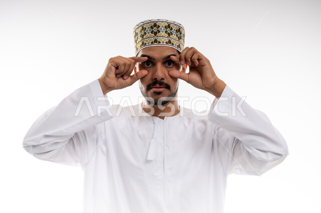 الوقوف امام الكاميرا وأداء حركات تمثيليه، بورتريه لرجل عربي خليجي عماني يرتدي الدشداشة التقليدية والكمه العمانية يضع يديه على عينيه بشكل دائري بتمثيل حركه المنظار، التأمل بتحقيق الأحلام والطموحات ورؤية الخطط المستقبلية، خلفية بيضاء