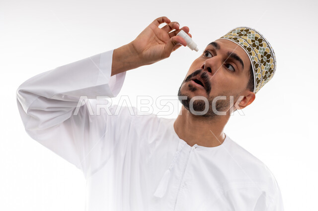 ارتفاع ضغط العين, الاحساس بالجفاف و احمرار العيون، الحاجة للفحص وعلاج حالات التهاب القرنيه، بورتريه لرجل عربي خليجي عماني يرتدي الدشداشه والكمه يقوم بوضع قطرة عينية, خلفية بيضاء