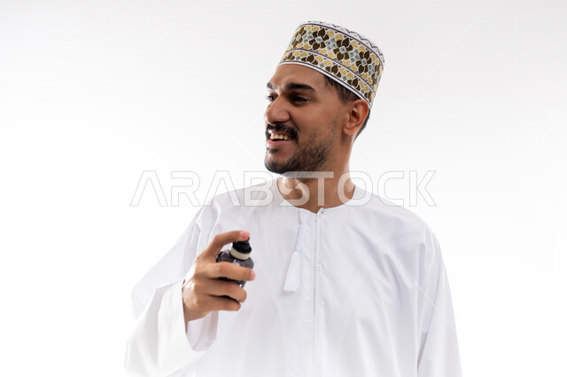 Using natural essential oils, Arabian Gulf perfumes, the concept of elegance and interest in one's appearance, a portrait of an Arabian Gulf Omani man wearing a dishdasha and a kuma spraying perfume on his robe, marketing perfume products, white background