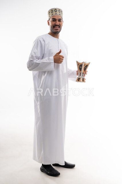 استخدام خشب العود بالأعياد والمناسبات, التطيب بالعطور والبخور, بورتريه لشاب عربي خليجي عماني يرتدي الدشداشه والكمه يحمل بيده المبخرة ويقوم بالتعطر, الأناقة والاهتمام بالمظهر الخارجي, العادات والتقاليد العمانيه, خلفيه بيضاء