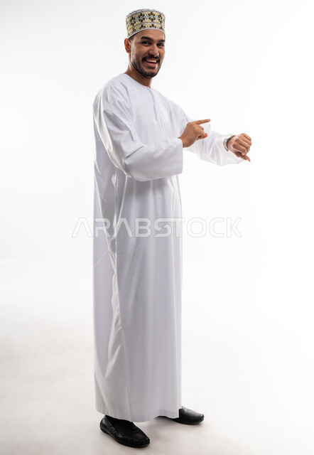 The concept of the importance of time and commitment to appointments, a portrait of an Arab Gulf Omani man wearing a dishdasha and a kummah looking at his personal watch with gestures of the importance of commitment to time and completing tasks and work accurately, white background