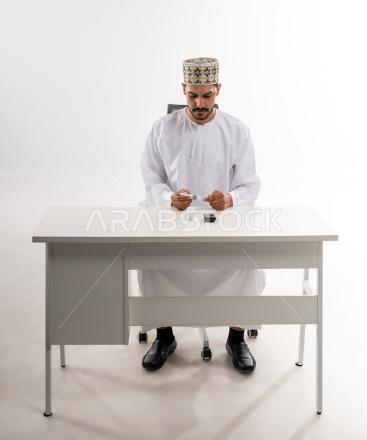 Physical pain and medical conditions, high blood sugar problems, portrait of an Arab Gulf Omani man wearing a dishdasha and a sleeve checking his blood sugar level using a rapid testing device, modern electronic devices for diabetics, white background