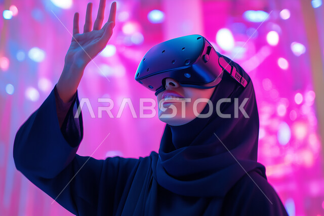 الاندماج والتفاعل مع العناصر الهولوجرامية، تقنيات حديثة الكترونية وأجهزة تكنولوجية، صورة مقربة لامرأة عربية خليجية سعودية محجبة ترتدي العباءة التقليدية تقف وترفع يدها للأعلى في محاولة للمس المكونات الخيالية، ارتداء نظارات الواقع الافتراضي الفي ار، خلفية ملونة