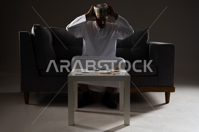 معاقبة النفس وتأنيب الضمير، المعاناة من الاضطرابات النفسية والمشاكل الصحية، بورتريه لرجل عربي خليجي عماني يرتدي الدشداشه والكمه يجلس على الاريكة يقوم بالاستعداد لتناول المواد المخدره، الآثار السلبية للادمان والتعاطي، القيام بعادات سلوكية ضارة وتعاطي المواد السامة، صوره ظليه