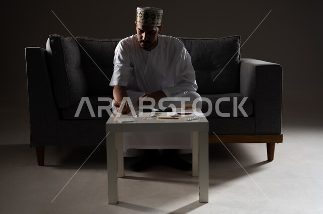 القيام بعادات سلوكية ضارة وتعاطي المواد السامة، الأثار السلبية للادمان على التبغ والمخدرات، المعاناة من الاضطرابات النفسية والمشاكل الصحية، بورتريه لرجل عربي خليجي عماني يرتدي الدشداشه والكمه يجلس على اريكة وييكشف عن ذراعه استعدادا لحقن المواد المخدره، صوره ظليه