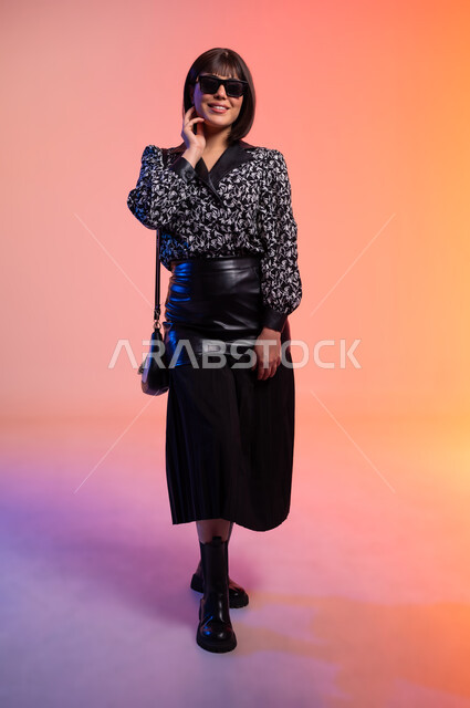 Features of femininity and softness, modern women's clothing, close-up portrait of a Saudi Arabian Gulf woman wearing sunglasses, putting her hand on her cheek with gestures of confidence, concept of fashion and elegance, fashion show and modern models, buying new accessories, full-length body, colorful background