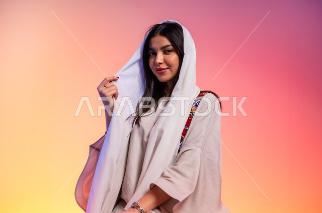 عرض الأزياء والموديلات الحديثة، ملامح الانوثة والنعومة, ألبسة خليجية نسائية عصرية، بورتريه مقرب لامرأة عربية خليجية سعودية ترتدي عباءة بيج تنظر إلى مكان ما بايماءات الخجل والحياء، مفهوم الموضة والأناقة، شراء الملابس والاكسسوارات الجديدة، خلفية ملونة