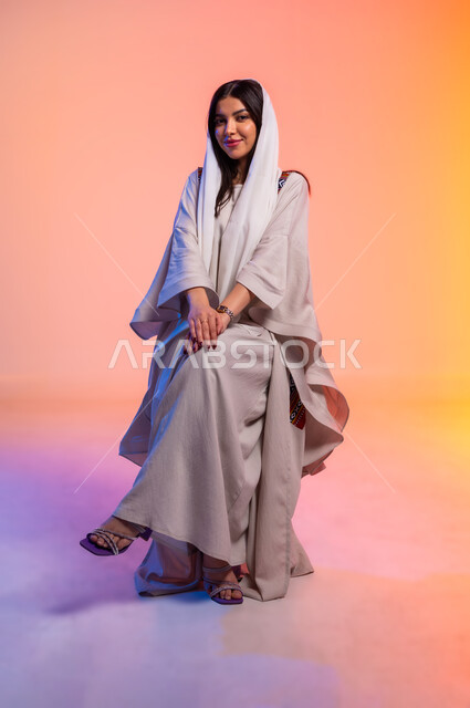 ملامح النعومة والانوثة, ألبسة خليجية نسائية عصرية، بورتريه لامرأة عربية خليجية سعودية محجبة ترتدي عباءة باللون البيج تنظر بتعابير الخجل والحياء، مفهوم الموضة والأناقة، عرض الأزياء والموديلات الحديثة، شراء الملابس والاكسسوارات الجديدة، خلفية ملونة