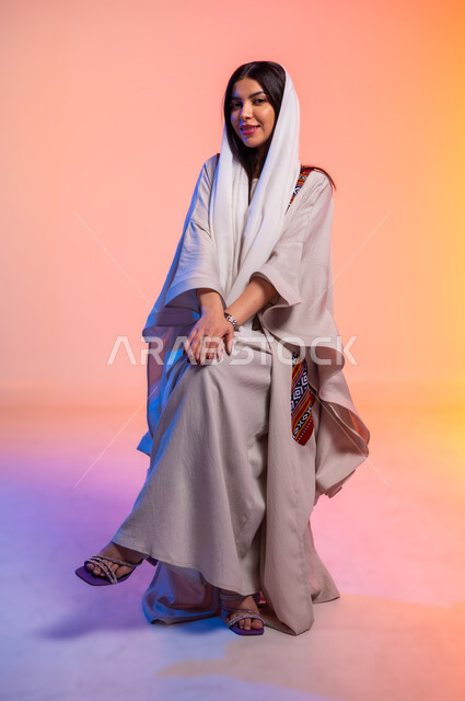 ملامح النعومة والانوثة, ألبسة خليجية نسائية عصرية، بورتريه لامرأة عربية خليجية سعودية محجبة ترتدي عباءة باللون البيج تنظر بتعابير الخجل والحياء، مفهوم الموضة والأناقة، عرض الأزياء والموديلات الحديثة، شراء الملابس والاكسسوارات الجديدة، خلفية ملونة