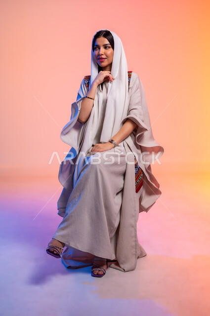 ملامح النعومة والانوثة, ألبسة خليجية نسائية عصرية، بورتريه لامرأة عربية خليجية سعودية محجبة ترتدي عباءة باللون البيج تنظر بتعابير الخجل والحياء، مفهوم الموضة والأناقة، عرض الأزياء والموديلات الحديثة، شراء الملابس والاكسسوارات الجديدة، خلفية ملونة