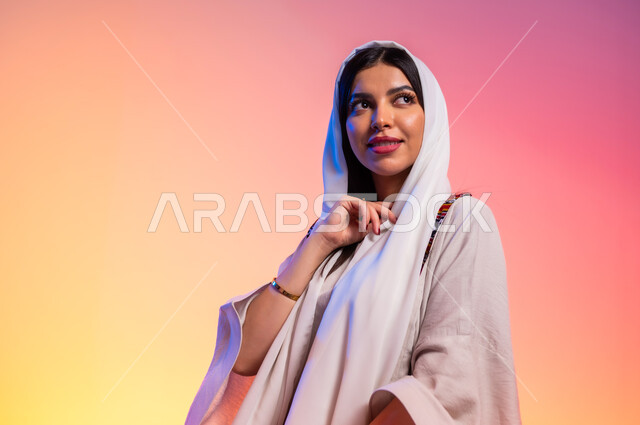 عرض الأزياء والموديلات الحديثة، ملامح الانوثة والنعومة, ألبسة خليجية نسائية عصرية، بورتريه مقرب لامرأة عربية خليجية سعودية ترتدي عباءة بيج تنظر إلى مكان ما بايماءات الخجل والحياء، مفهوم الموضة والأناقة، شراء الملابس والاكسسوارات الجديدة، خلفية ملونة