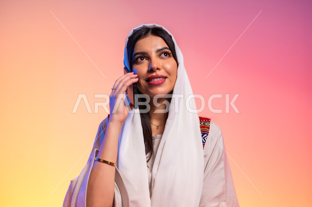 Features of femininity and softness, modern Gulf women's clothing, close-up portrait of a Saudi Gulf Arab woman wearing a beige abaya making a phone call via mobile phone, concept of fashion and elegance, fashion show and modern models, buying new clothes and accessories, colorful background