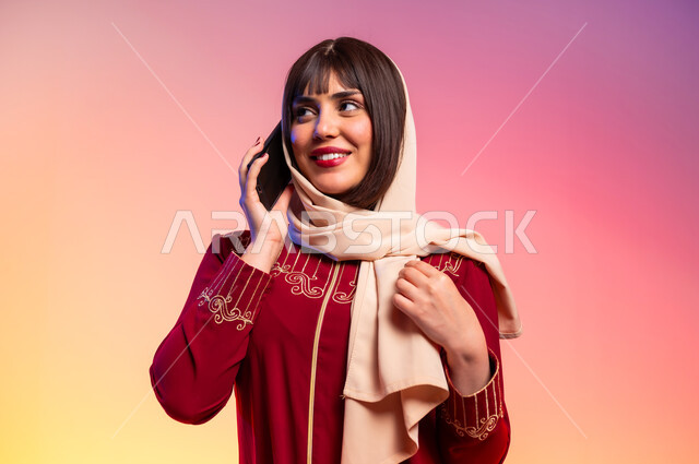 التواصل مع الاهل والاصدقاء باستخام الموبايل, ألبسة خليجية نسائية عصرية، بورتريه لامرأة عربية خليجية سعودية تحمل الهاتف المحمول وتقوم باجراء مكالمة هاتفية، مفهوم الموضة والأناقة، عرض الأزياء والموديلات الحديثة، شراء الملابس والاكسسوارات الجديدة، خلفية ملونة