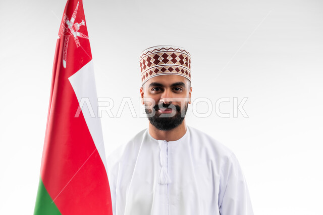 الفخر والاعتزاز بالانتماء للهوية، المشاركة بالاعياد والمناسبات الوطنية، الاحتفال بذكرى اليوم الوطني العماني، الاعتزاز والفخر بالرموز والراية العمانية، بورتريه لشاب عربي خليجي عماني يرتدي الدشداشة والكمه، مفهوم حب الوطن، خلفية بيضاء