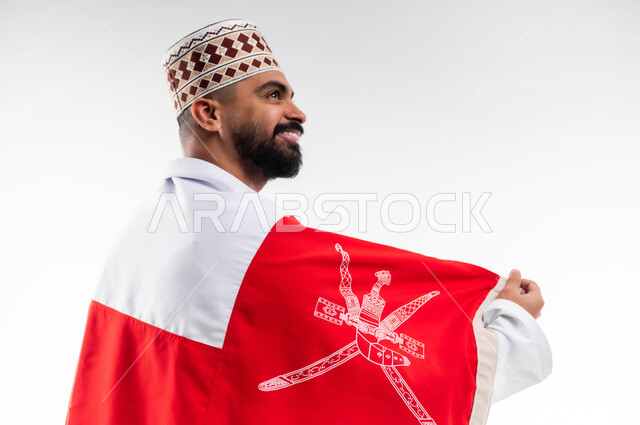 الفخر والاعتزاز بالانتماء للهوية، المشاركة بالاعياد والمناسبات الوطنية، الاحتفال بذكرى اليوم الوطني العماني، الاعتزاز والفخر بالرموز والراية العمانية، بورتريه لشاب عربي خليجي عماني يرتدي الدشداشة والكمه، مفهوم حب الوطن، خلفية بيضاء