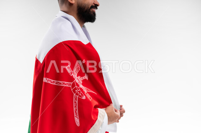 Pride and honor of belonging to the identity, participation in national holidays and occasions, celebration of the Omani National Day, pride and honor of the Omani symbols and flag, portrait of a young Arab Gulf Omani man wearing a dishdasha and a kuma, the concept of patriotism, white background