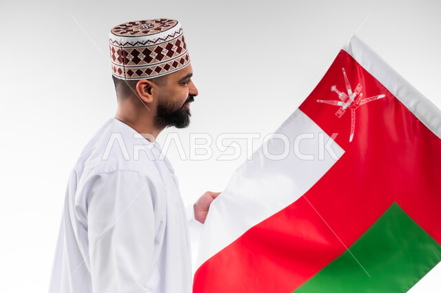 الفخر والاعتزاز بالانتماء للهوية، المشاركة بالاعياد والمناسبات الوطنية، الاحتفال بذكرى اليوم الوطني العماني، الاعتزاز والفخر بالرموز والراية العمانية، بورتريه لشاب عربي خليجي عماني يرتدي الدشداشة والكمه، مفهوم حب الوطن، خلفية بيضاء