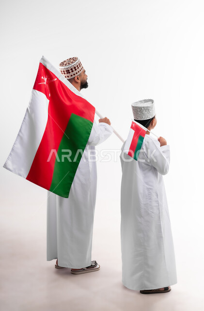 الاحتفال بذكرى اليوم الوطني العماني، الرايات والأعلام الوطنية للدول العربية، الاعتزاز والفخر بالرموز والراية العمانية، بورتريه لطفل وشاب عربي خليجي عماني يرتدي الدشداشة والكمه، مفهوم حب الوطن والإنتماء إليه، الجسم بالطول الكامل، خلفية بيضاء