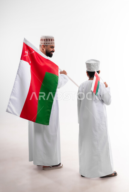 Celebrating Oman National Day, national flags and banners of Arab countries, pride in Omani symbols and banner, portrait of an Arab Gulf Omani boy and young man wearing a dishdasha and a kuma, the concept of love of the homeland and belonging to it, full body, white background