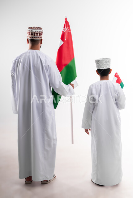 الاحتفال بذكرى اليوم الوطني العماني، الرايات والأعلام الوطنية للدول العربية، الاعتزاز والفخر بالرموز والراية العمانية، بورتريه لطفل وشاب عربي خليجي عماني يرتدي الدشداشة والكمه، مفهوم حب الوطن والإنتماء إليه، الجسم بالطول الكامل، خلفية بيضاء