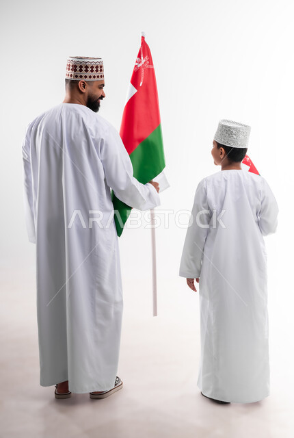 الاحتفال بذكرى اليوم الوطني العماني، الرايات والأعلام الوطنية للدول العربية، الاعتزاز والفخر بالرموز والراية العمانية، بورتريه لطفل وشاب عربي خليجي عماني يرتدي الدشداشة والكمه، مفهوم حب الوطن والإنتماء إليه، الجسم بالطول الكامل، خلفية بيضاء