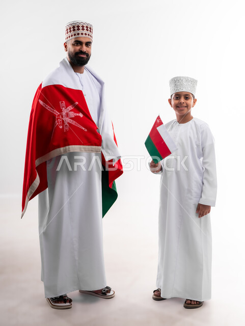 الاحتفال بذكرى اليوم الوطني العماني، الرايات والأعلام الوطنية للدول العربية، الاعتزاز والفخر بالرموز والراية العمانية، بورتريه لطفل وشاب عربي خليجي عماني يرتدي الدشداشة والكمه، مفهوم حب الوطن والإنتماء إليه، الجسم بالطول الكامل، خلفية بيضاء