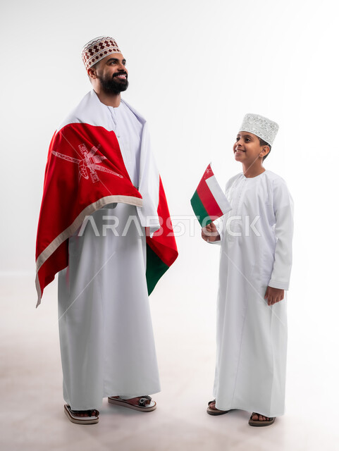 الاحتفال بذكرى اليوم الوطني العماني، الرايات والأعلام الوطنية للدول العربية، الاعتزاز والفخر بالرموز والراية العمانية، بورتريه لطفل وشاب عربي خليجي عماني يرتدي الدشداشة والكمه، مفهوم حب الوطن والإنتماء إليه، الجسم بالطول الكامل، خلفية بيضاء
