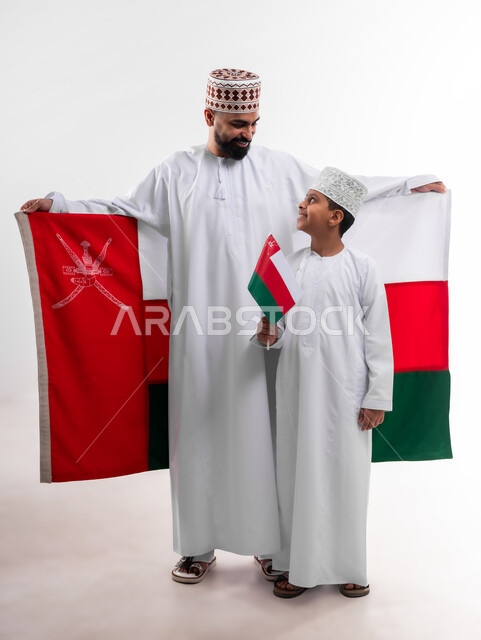 الاحتفال بذكرى اليوم الوطني العماني، الرايات والأعلام الوطنية للدول العربية، الاعتزاز والفخر بالرموز والراية العمانية، بورتريه لطفل وشاب عربي خليجي عماني يرتدي الدشداشة والكمه، مفهوم حب الوطن والإنتماء إليه، الجسم بالطول الكامل، خلفية بيضاء