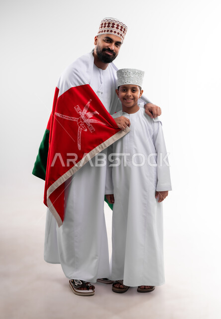 الاحتفال بذكرى اليوم الوطني العماني، الرايات والأعلام الوطنية للدول العربية، الاعتزاز والفخر بالرموز والراية العمانية، بورتريه لطفل وشاب عربي خليجي عماني يرتدي الدشداشة والكمه، مفهوم حب الوطن والإنتماء إليه، الجسم بالطول الكامل، خلفية بيضاء