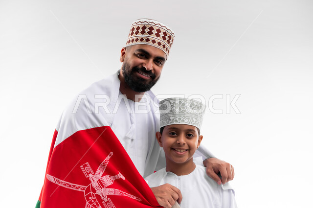 الاحتفال بذكرى اليوم الوطني العماني، الرايات والأعلام الوطنية للدول العربية، الاعتزاز والفخر بالرموز والراية العمانية، بورتريه مقرب لطفل وشاب عربي خليجي عماني يرتدي الدشداشة والكمه، مفهوم حب الوطن والإنتماء إليه، خلفية بيضاء
