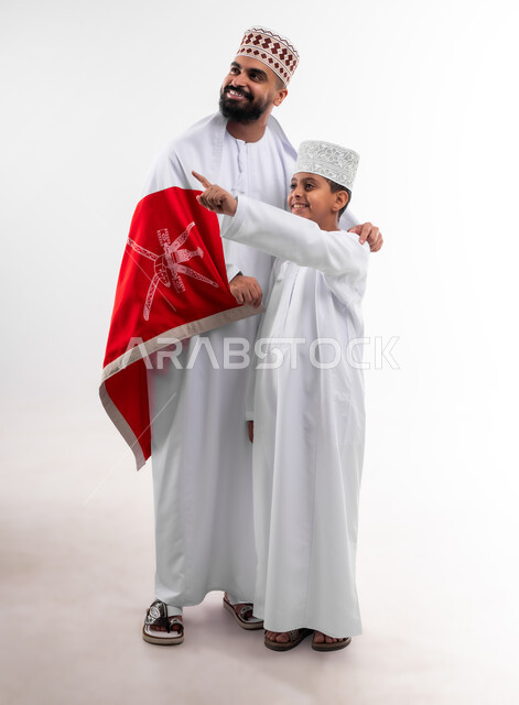 الاحتفال بذكرى اليوم الوطني العماني، الرايات والأعلام الوطنية للدول العربية، الاعتزاز والفخر بالرموز والراية العمانية، بورتريه لطفل وشاب عربي خليجي عماني يرتدي الدشداشة والكمه، مفهوم حب الوطن والإنتماء إليه، الجسم بالطول الكامل، خلفية بيضاء
