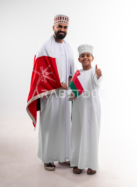 الاحتفال بذكرى اليوم الوطني العماني، الرايات والأعلام الوطنية للدول العربية، الاعتزاز والفخر بالرموز والراية العمانية، بورتريه لطفل وشاب عربي خليجي عماني يرتدي الدشداشة والكمه، مفهوم حب الوطن والإنتماء إليه، الجسم بالطول الكامل، خلفية بيضاء