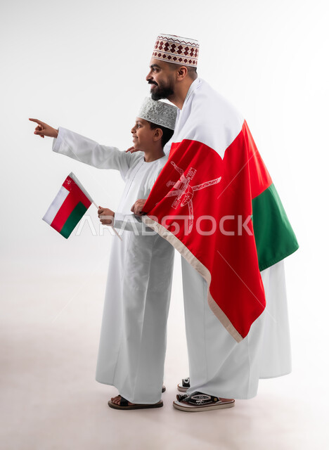 الاحتفال بذكرى اليوم الوطني العماني، الرايات والأعلام الوطنية للدول العربية، الاعتزاز والفخر بالرموز والراية العمانية، بورتريه لطفل وشاب عربي خليجي عماني يرتدي الدشداشة والكمه، مفهوم حب الوطن والإنتماء إليه، الجسم بالطول الكامل، خلفية بيضاء