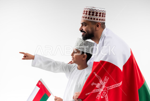 الاحتفال بذكرى اليوم الوطني العماني، الرايات والأعلام الوطنية للدول العربية، الاعتزاز والفخر بالرموز والراية العمانية، بورتريه مقرب لطفل وشاب عربي خليجي عماني يرتدي الدشداشة والكمه، مفهوم حب الوطن والإنتماء إليه، خلفية بيضاء