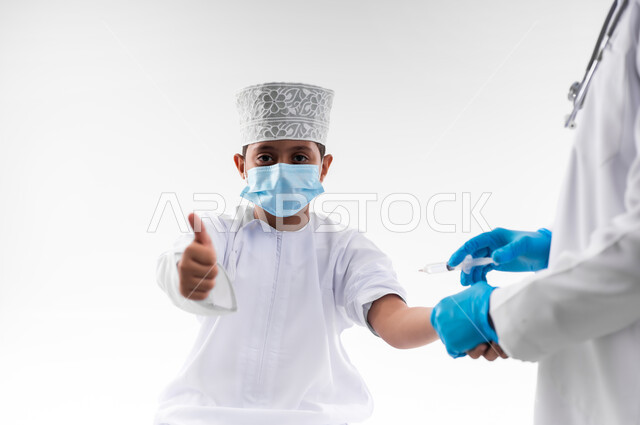 اتباع قوانين وزارة الصحة، اتاحة تلقي التطعيم ضد فايروس كورونا للاطفال، بورتريه مقرب لطبيب يرتدي المعطف والقفازات الطبية، يقوم باعطاء جرعة لقاح كوفيد - 19 لطفل عربي خليجي عماني، الالتزام بإجراءات السلامة، خلفية بيضاء
