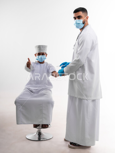 The availability of vaccination against the Corona virus for children, a portrait of a doctor wearing the coat and medical gloves, gives the dose of the Kofid vaccine - 19 to an Arab Gulf Arab child, adhering to safety procedures, following the laws of the Ministry of Health, body with full length, white background
